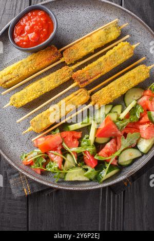 Aliments sains bâtonnets d’aubergines boulonnées servis avec une salade de légumes et une sauce tomate gros plan sur une assiette sur une table en bois. Vue de dessus verticale Banque D'Images