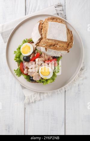 Sandwich French Pan Bagnat avec salade nicoise dans du pain de seigle spécial gros plan sur une assiette sur une table en bois. Vue de dessus verticale Banque D'Images