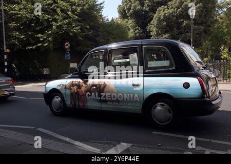 Taxi noir avec publicité pour Italian Beachwear sur la route à l'extérieur de Rose Square Fulham Road Chelsea Londres Angleterre Banque D'Images