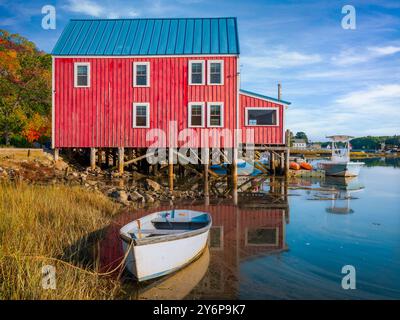 Bâtiment en bois rouge sur pilotis se trouve au bord d'un front de mer calme, avec de petits bateaux amarrés à proximité. La scène comprend des reflets dans l'eau et v Banque D'Images