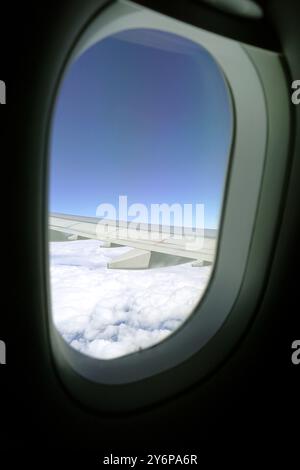 Voyager en avion : une fenêtre et une vue à travers elle de l'aile d'un avion volant au-dessus des nuages. Photo prise lors d'un vol par temps nuageux. Banque D'Images
