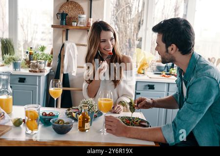 Cœurs remplis d'amour. Beau jeune couple profitant d'un petit déjeuner sain tout en étant assis dans la cuisine à la maison Banque D'Images