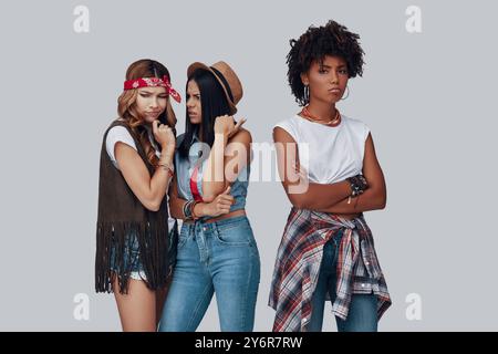 Deux jeunes femmes bavardant derrière leur copine en arrière tout en se tenant debout sur fond gris Banque D'Images