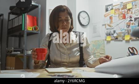 Une détective hispanique examine les preuves dans le bureau encombré d'un département de police à l'intérieur. Banque D'Images