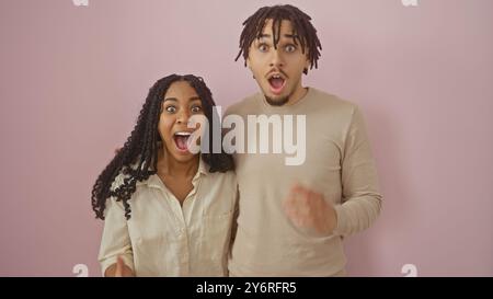 Couple excité avec une femme et un homme exprimant la surprise contre un mur rose Uni Banque D'Images
