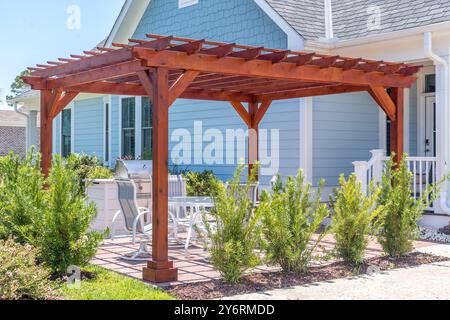 Structure d'ombre de pergola de patio extérieur tendance en bois sombre, auvent et toit de patio, table à manger blanche, chaises blanches, grill en métal Banque D'Images