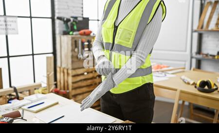 Artisan en gilet réfléchissant se préparant dans un atelier de menuiserie bien équipé. Banque D'Images