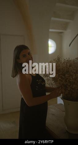 Jeune, hispanique, femme debout dans une maison italienne rustique arrangeant des fleurs séchées avec le sourire. Banque D'Images