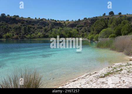 Un lac calme avec une eau bleu clair, entouré d'arbres verts et de collines ondulantes sous un ciel clair, Laguna Santo Morcillo, Lagunas de Ruidera National P Banque D'Images