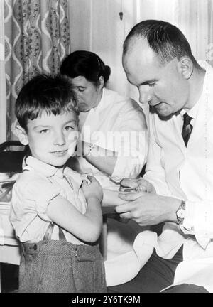 HULL, Yorkshire : Nicholas Pearcy, neuf ans, tient la manche tandis que le Dr Garey se prépare à lui faire une injection anti-polio à la clinique Collman Street à Hull hier. Il y a eu une augmentation alarmante du nombre de victimes de poliomyélite dans la ville au cours des dernières semaines, 15 nouveaux cas depuis la fin septembre. Mercredi prochain, pour la première fois en Grande-Bretagne, une vaccination orale de masse sera administrée. Le nouveau vaccin recevra deux gouttes à la fois sur des morceaux de sucre et il est revendiqué pour donner une protection immédiate. 14 OCTOBRE 1961 Banque D'Images