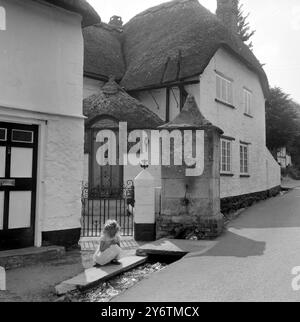 Les rêves deviennent réalité pour Susan Hansford, six ans de Beer , South Devon comme se prélasser dans la lumière du soleil du matin , elle regarde et rêve dans le petit ruisseau qui coule devant cette belle chaume cottage dans la rue principale de Beer . Ancienne pompe à eau chevauche le petit ruisseau. 1961 Banque D'Images