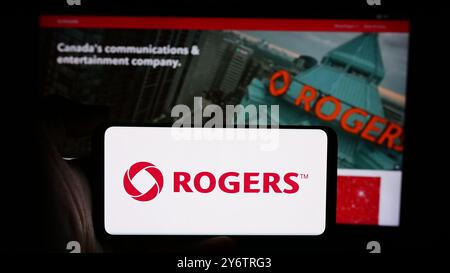 Dans cette illustration photo, une personne tient un téléphone cellulaire avec le logo de la société de communications canadienne Rogers Communications Inc devant la page Web. Banque D'Images