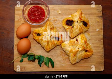 Gros plan sur une planche à découper en feuilletés aux œufs savoureux de style Kerala avec sauce tomate, feuilles de curry et oeuf. Fond en bois Banque D'Images