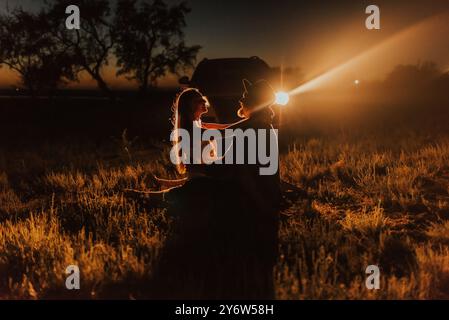 couple de jeunes amoureux sont assis sur le sol face à l'autre serrant sur fond de voiture avec les phares allumés. dans les rayons lumineux de fond. Banque D'Images