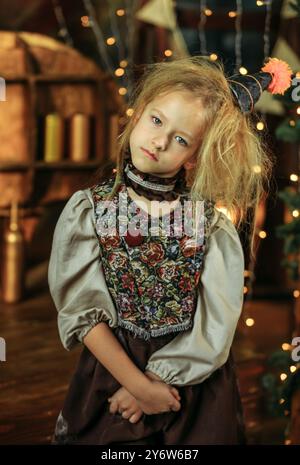 Une jeune fille se tient devant un arbre de Noël décoré, regardant dans la crainte devant les lumières scintillantes et les ornements colorés. Banque D'Images