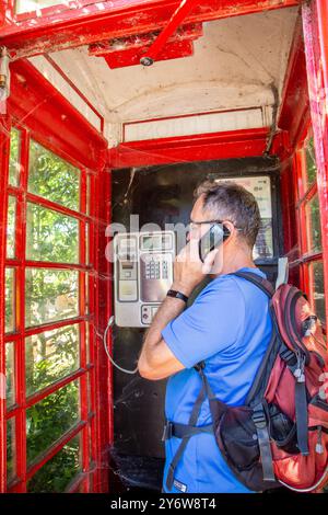 Homme discutant en utilisant un téléphone dans un kiosque traditionnel rouge anglais de cabine téléphonique n ° 6 / K6 conçu en 1935 par Sir Gilbert Scott Banque D'Images