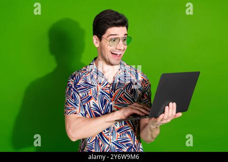 Photo du gars impressionné avec la chemise habillée habillée de poils coiffés dans les lunettes regarder l'ordinateur portable hp isolé sur fond de couleur verte Banque D'Images