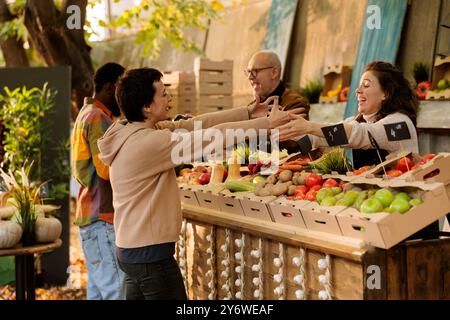 Un fournisseur local enthousiaste accueille son client favori sur le stand greenmarket avec des produits bio biologiques. Happy Farmer accueille le client et vend des fruits et légumes cultivés sur le stand de foire agricole respectueux de l'environnement. Banque D'Images