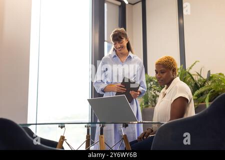 Collaborant au bureau, deux femmes utilisant un ordinateur portable et une tablette numérique au bureau Banque D'Images