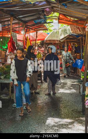 Balikpapan, Indonésie - 26 juin 2024. Accompagnés de ses autres filles, ils marchent à travers le marché traditionnel boueux de Pandan Sari. Banque D'Images