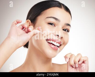 Femme, soie dentaire et portrait en studio pour les soins dentaires, l'hygiène et la routine pour l'haleine fraîche. Personne, heureux et ficelle sur fond gris pour la plaque Banque D'Images