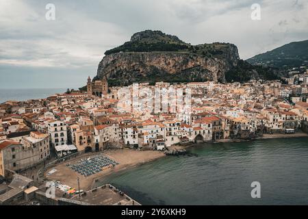 Vue aérienne de Cefalu, Sicile, avec des bâtiments historiques et une plage, sur fond montagneux et ciel couvert. Banque D'Images