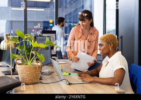 Collaborant au bureau, deux femmes utilisant un ordinateur portable et des documents discutant du projet Banque D'Images