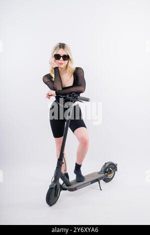 Femme monter e-scooter regardant la caméra isolée sur un portrait de studio de fond blanc. Concept de style de vie Banque D'Images