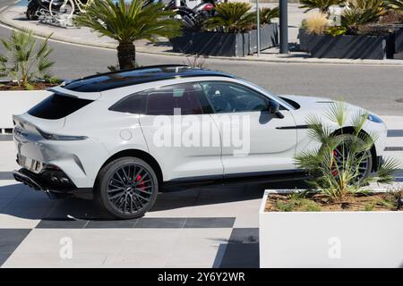 White aston martin dbx est garé sur un trottoir à carreaux près de palmiers par une journée ensoleillée Banque D'Images