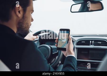 Vérifier le bon chemin. Vue arrière d'un jeune homme à l'aide d'un téléphone intelligent pour vérifier la carte tout en conduisant une voiture Banque D'Images