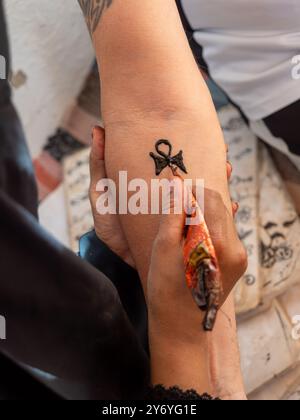 Une femme dessine un tatouage avec du henné sur le bras d'une femme. Le tatouage est d'un symbole égyptien, et la femme utilise un pinceau de henné pour le créer. Scène Banque D'Images