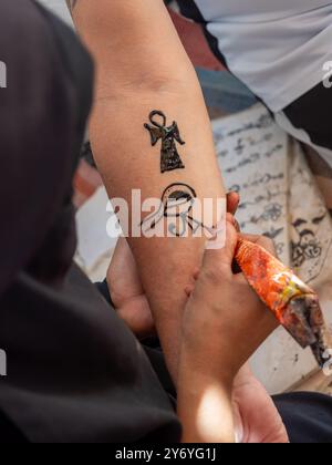 Une femme nubienne dessine un tatouage avec du henné sur le bras d'une femme. Le tatouage est d'un symbole égyptien, et la femme utilise un pinceau de henné pour le créer Banque D'Images