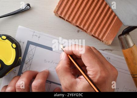 Détail de l'architecte notant sur le plan de la maison sur la table en bois blanc avec des outils et des matériaux de construction. Vue de dessus. Banque D'Images