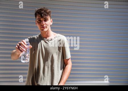 Jeune homme beau tend une main avec une bouteille d'eau Banque D'Images