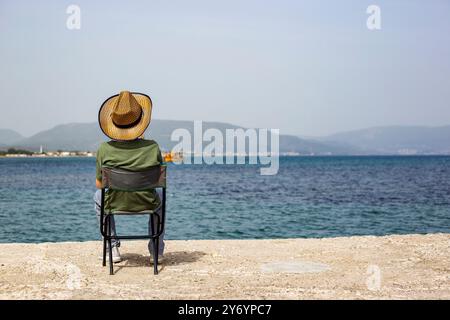 Vue arrière d'une personne assise sur une chaise par l'horizon de la mer waching Banque D'Images