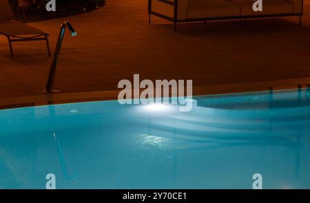 Détendez-vous au bord d'une piscine éclairée la nuit, son eau bleue scintillante sous une lumière douce, créant une oasis de paix parfaite pour se détendre et échapper à l'agitation quotidienne Banque D'Images