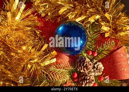 Une décoration de Noël colorée et festive, avec une boule bleu vif entourée d'un noeud rouge étincelant, de pommes de pin et de branches à feuilles persistantes Banque D'Images