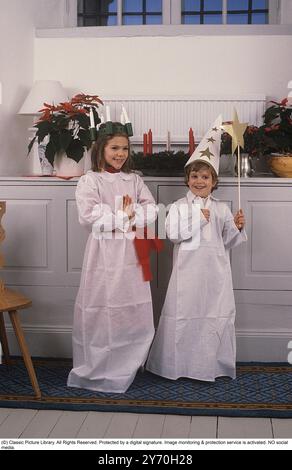 Princesse héritière Victoria et son frère le prince Carl Philippe de Suède 1984. Vêtu d'une tenue traditionnelle lors de la célébration de la Saint Lucy le 13 décembre. On voit la reine Silvia aider sa fille à s'habiller. Banque D'Images