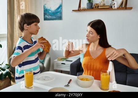 Un jeune garçon malentendant prend son petit déjeuner avec sa mère, partageant des gestes significatifs. Banque D'Images