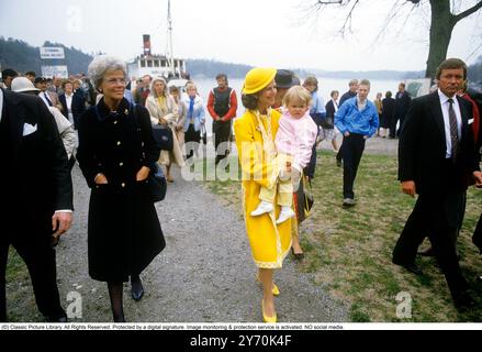 Reine Silvia de Suède photographiée dans un manteau jaune et un chapeau jaune assorti tenant sa fille princesse Madeleine lors de la cérémonie de remise du nom du navire M / S Mälar Victoria 1984. Banque D'Images