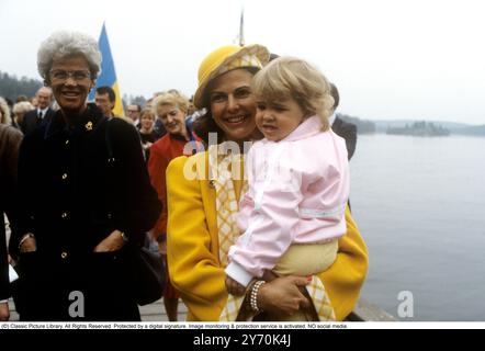 Reine Silvia de Suède photographiée dans un manteau jaune et un chapeau jaune assorti tenant sa fille princesse Madeleine lors de la cérémonie de remise du nom du navire M / S Mälar Victoria 1984. Banque D'Images