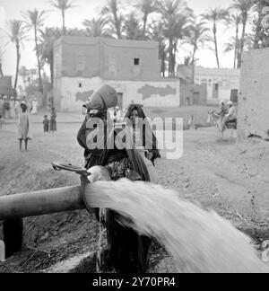 LE HAUT BARRAGE D'ASSOUAN APPROCHE DE L'ACHÈVEMENT ASSOUAN, EN ÉGYPTE ; les femmes égyptiennes portent leurs pots pour recueillir l'eau d'un pipeline du haut barrage. Bientôt, l'eau et l'électricité issues du projet conviendront à des millions d'Égyptiens. 28 janvier 1968 Banque D'Images