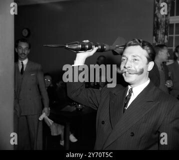 Des membres du club de guidons , dont Raymond Glendening , leur président , ont visité le Victory Club (ex-services) , à Seymour Street , Marble Arch , Londres , pour un match de fléchettes contre l'équipe du club . Une fléchette de quatre pieds a été mise à disposition pour le match. - - Spectacles de photos : M. Edward Hooker avec sa moustache de guidon de 9 1/3 pouces , lançant la fléchette de quatre pieds pendant le match . - - 18 juillet 1949 Banque D'Images