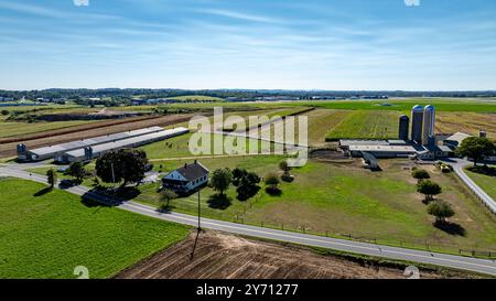 Une vaste étendue de terres agricoles sous un ciel bleu clair dispose de silos et d'une maison rurale pittoresque. Des champs luxuriants s'étendent au loin, mettant en valeur la beauté de la vie agricole. Banque D'Images