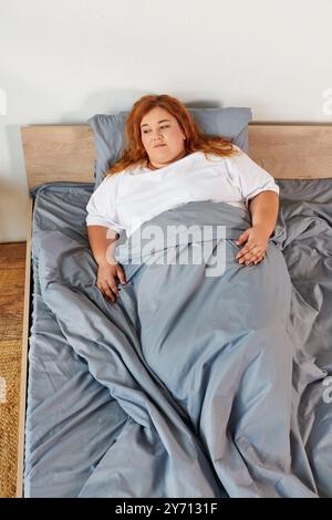 Une femme grande taille se repose confortablement sous des couvertures douces, profitant d'une matinée paisible au lit. Banque D'Images