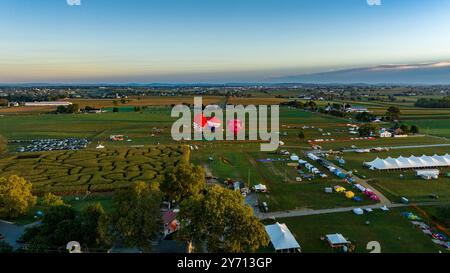 Bird in Hand, Pennsylvanie, États-Unis, 16 septembre 2023 - les montgolfières s'élèvent doucement au-dessus d'un paysage pittoresque rempli de champs et de tentes de festival, capturant l'esprit animé d'une célébration automnale alors que le soleil se couche en arrière-plan. Banque D'Images