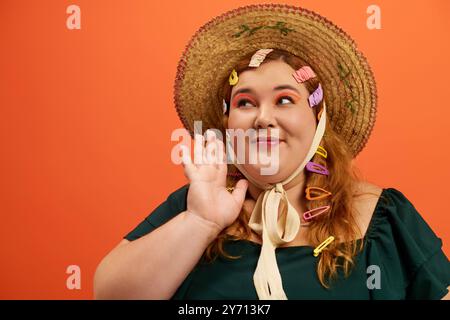 Une femme joyeuse de plus grande taille ondule tout en portant un grand chapeau de paille orné de clips colorés. Banque D'Images