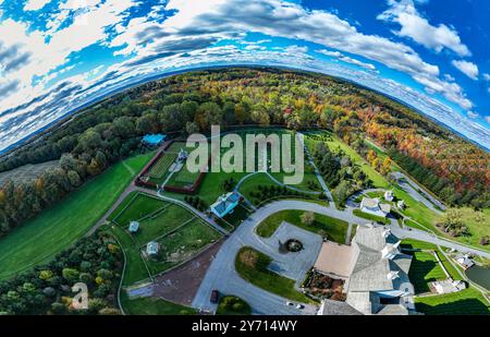 La scène capture une perspective aérienne époustouflante d'un paysage en automne, mettant en valeur un feuillage coloré, des jardins soigneusement agencés et un ciel bleu clair. Les arbres vibrants créent une toile de fond pittoresque. Banque D'Images