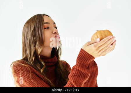 Une belle jeune femme dans une tenue colorée d'Halloween tient ludique une petite citrouille et sourit. Banque D'Images