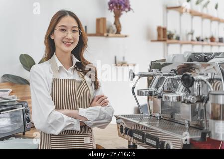 Heureuse jeune femme propriétaire de café debout derrière son comptoir à côté de sa machine à café souriant Banque D'Images